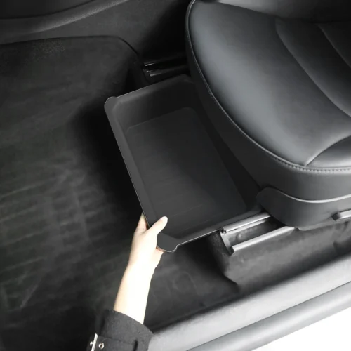 Person pulls out a black plastic tray from beneath a car seat, revealing a small storage bin