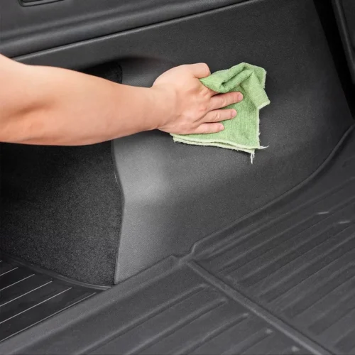 Person's hand wiping a car floor mat with a green cloth inside the vehicle