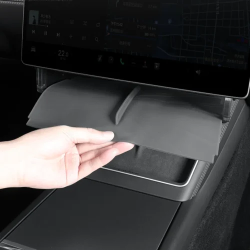 Hand lifting or pulling down a small storage tray from the center console beneath the car's touchscreen infotainment system.