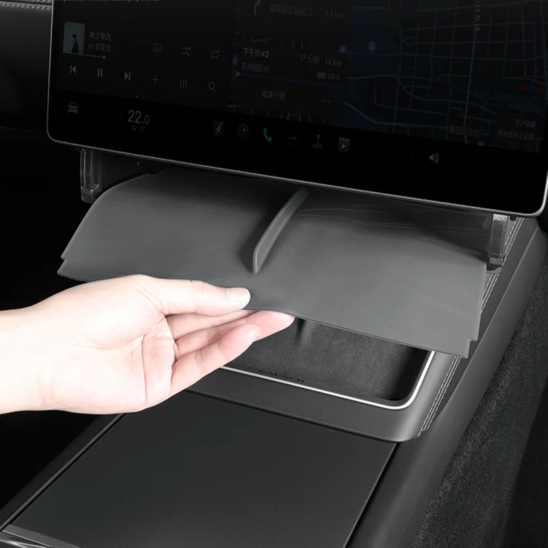 Hand lifting or pulling down a small storage tray from the center console beneath the car's touchscreen infotainment system.