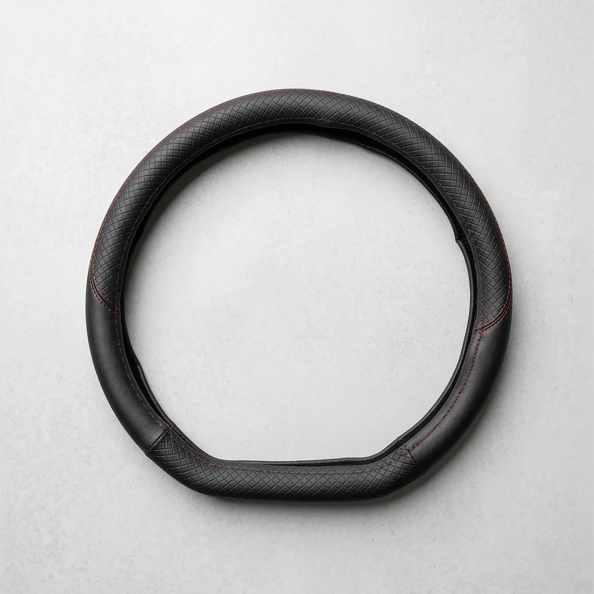 Black leather steering wheel cover, circular with red stitching, laid on a light gray surface.