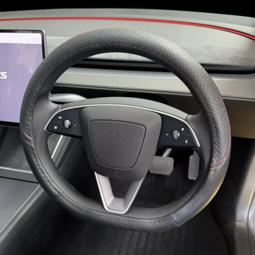 Close-up of a Tesla steering wheel with diamond-stitched grip, red stitching, and built-in controls; dashboard area visible.