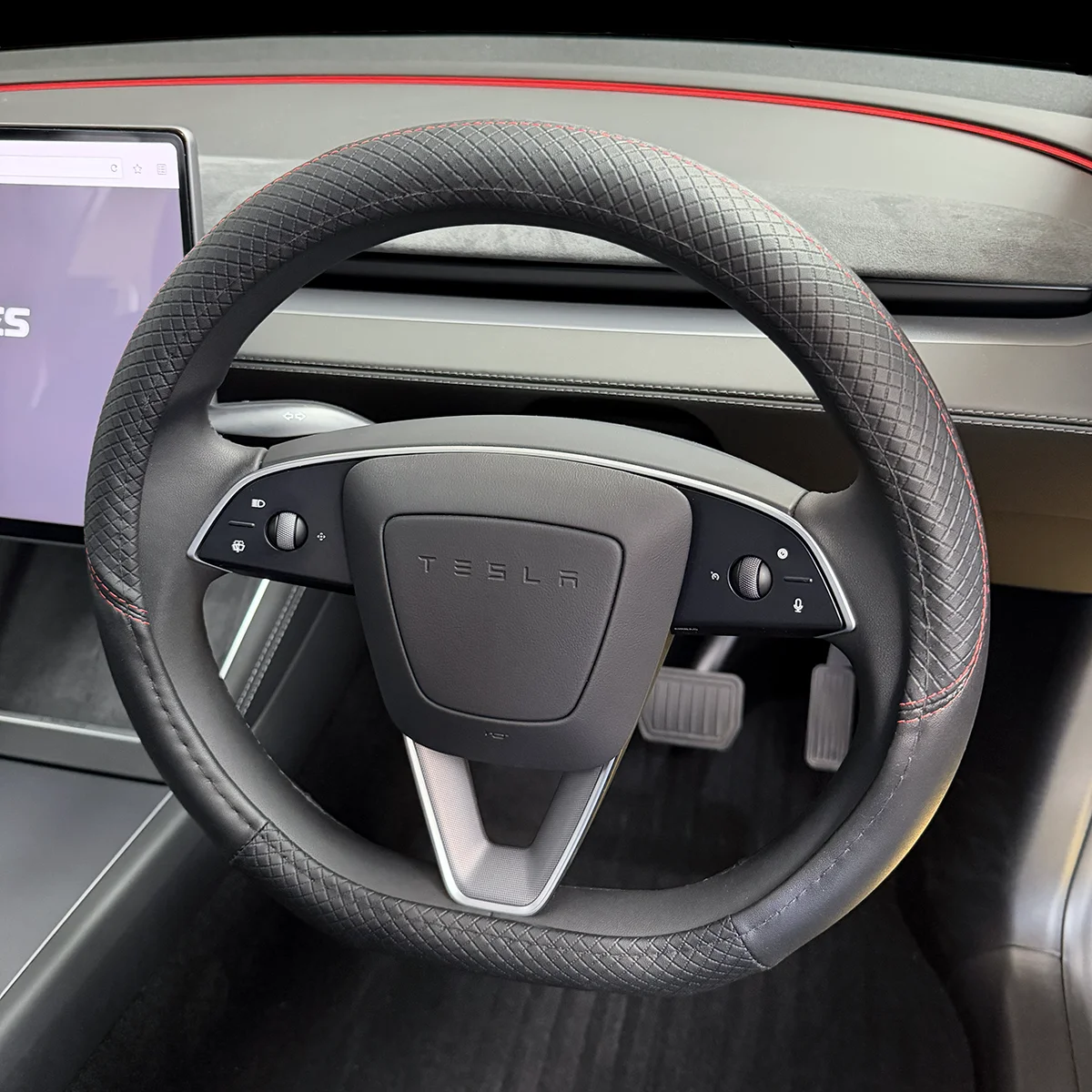 Close-up of a Tesla steering wheel with diamond-stitched grip, red stitching, and built-in controls; dashboard area visible.