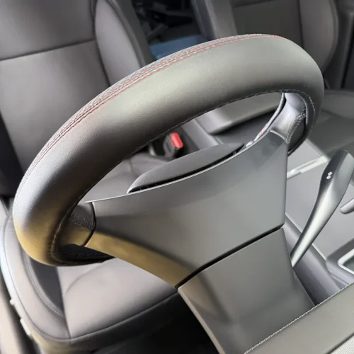 Close-up of a car steering wheel with red contrast stitching and a paddle shifter visible behind it, showing the premium interior detail.