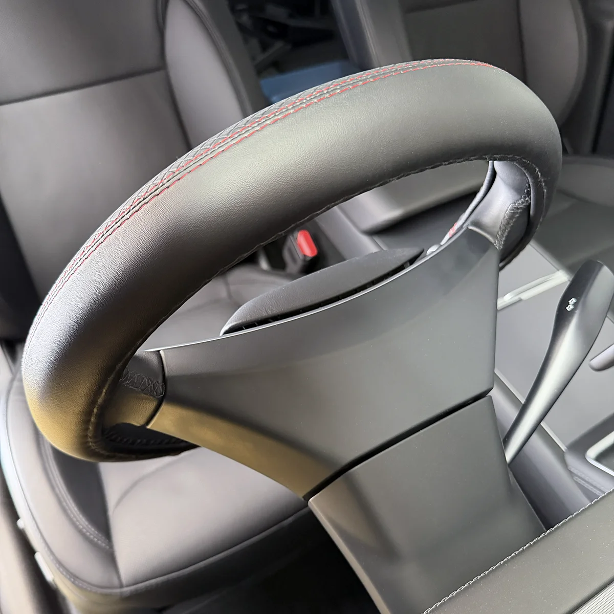 Close-up of a car steering wheel with red contrast stitching and a paddle shifter visible behind it, showing the premium interior detail.
