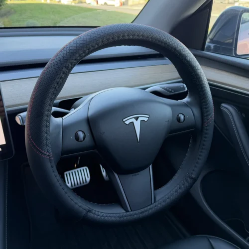 Tesla steering wheel with a textured black cover and red stitching in a car interior
