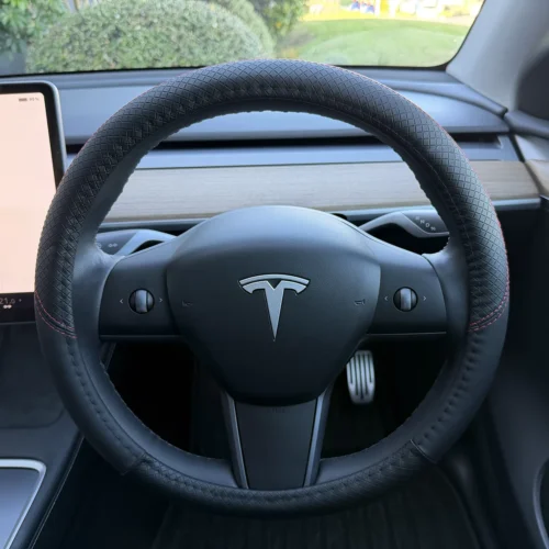 Tesla steering wheel with a diamond-pattern leather cover, centered logo, and partial view of the dashboard and left touchscreen.