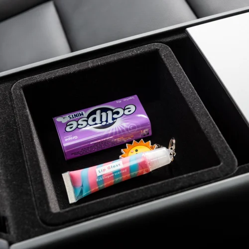 In a car's center console tray: a purple Eclipse mints tin, a striped Lip Gloss tube, and a sun-shaped keychain.