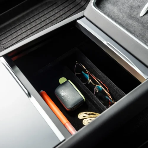 Open car center console drawer with a black organizer holding a pair of sunglasses, a car key fob, an orange pen, and gold hair clips.