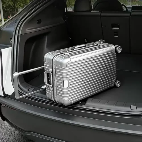 Silver hard-shell suitcase with wheels in the open trunk of an SUV, ready for loading or unloading.
