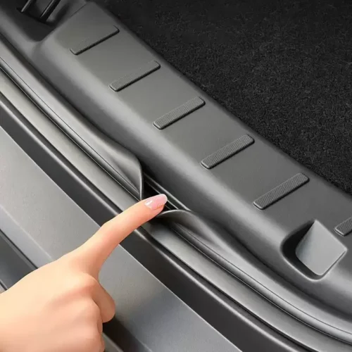 Close-up of a hand lifting the trunk sill trim along a car's cargo area edge.