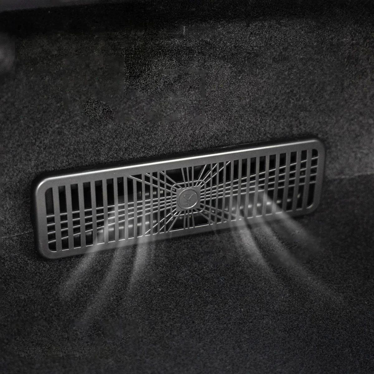 Rectangular ventilation grille mounted on a dark fabric surface, with a central hub and radial spokes.