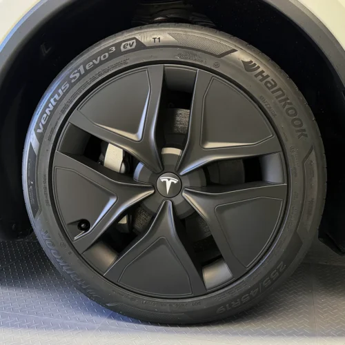 Close-up of a Tesla wheel with a dark aero-style rim and a Yokohama tire, featuring the Tesla logo at center.