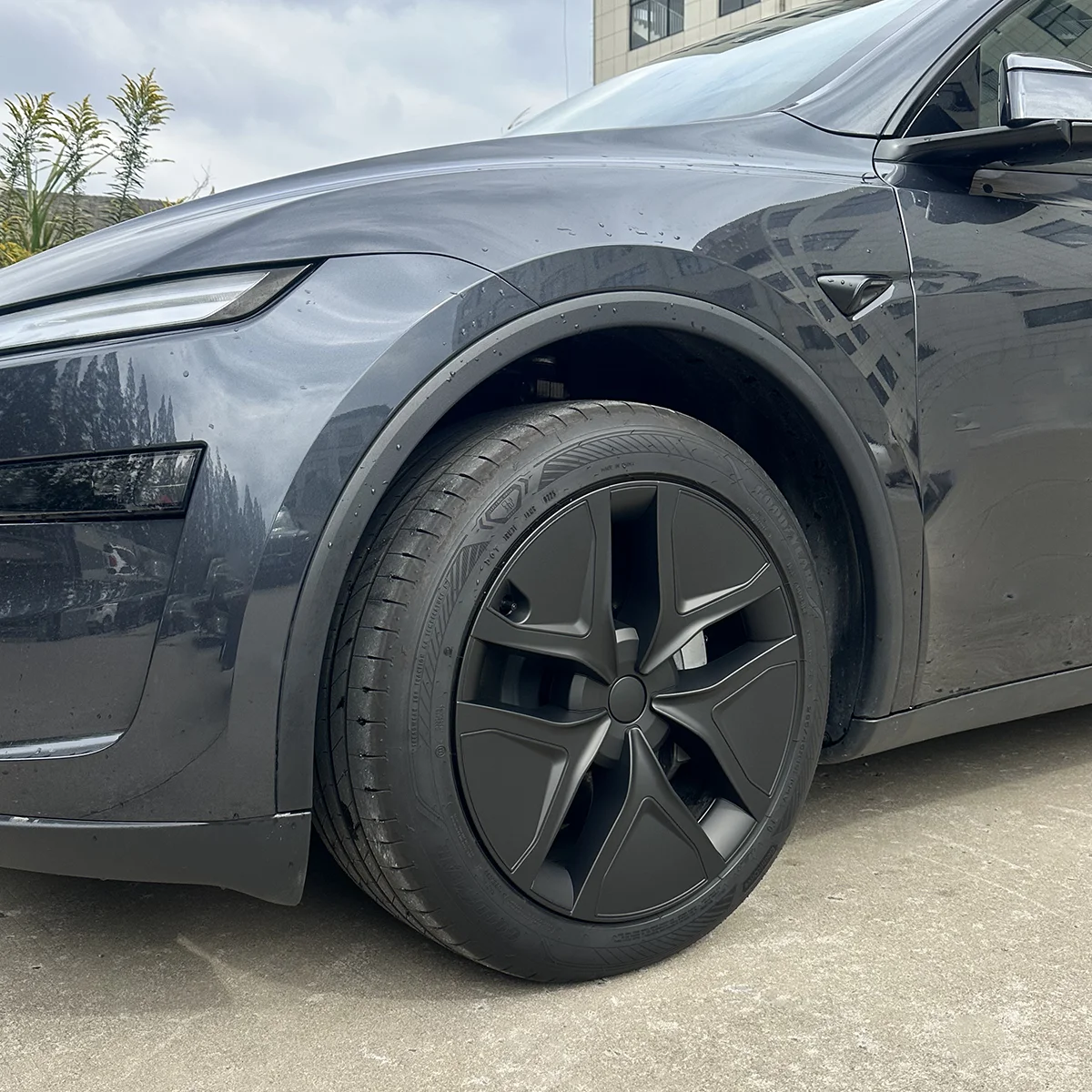 Close-up of a dark gray electric car's front left wheel with an aero wheel cover and curved fender.