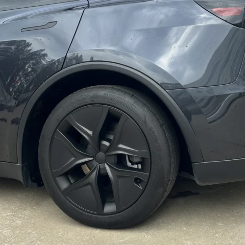 Close-up of a dark gray car's front wheel with a black alloy rim and Goodyear tire; wheel arch visible under the fender.